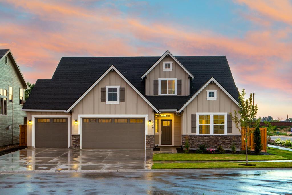 Modern farmhouse-style home photographed at dusk with warm interior lighting, neutral siding, and a neatly maintained front lawn.