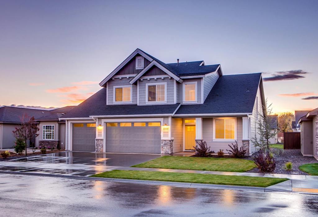 Two-story blue and gray suburban home photographed at twilight with warm interior lights and a clean, landscaped front yard.